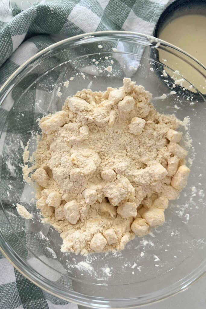 A glass bowl surrounded by a green and white checked dish towel. Inside the bowl there is flour and butter rubbed together to make sourdough puff pastry.