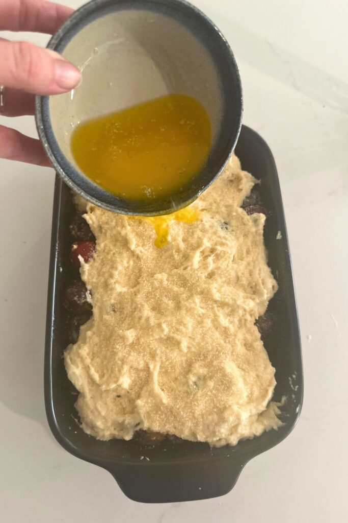 Pouring melted butter over the top of a sourdough cobbler.