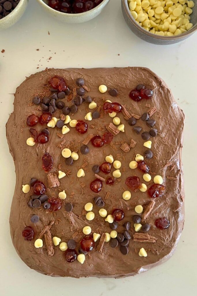 A rectangle of chocolate sourdough decorated with white and semi sweet chocolate chips and glace cherries.