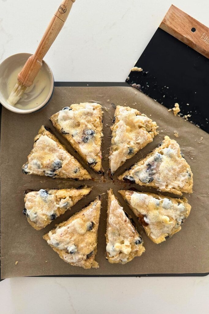 8 wedges of sourdough blueberry scone dough that have been brushed with heavy whipping cream and sprinkled with sugar.