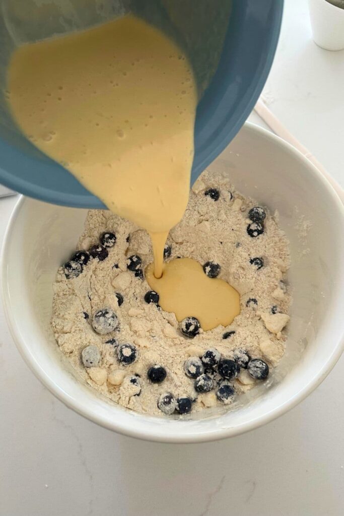 Liquid ingredients being poured into the dry ingredients in order to make sourdough blueberry scones.