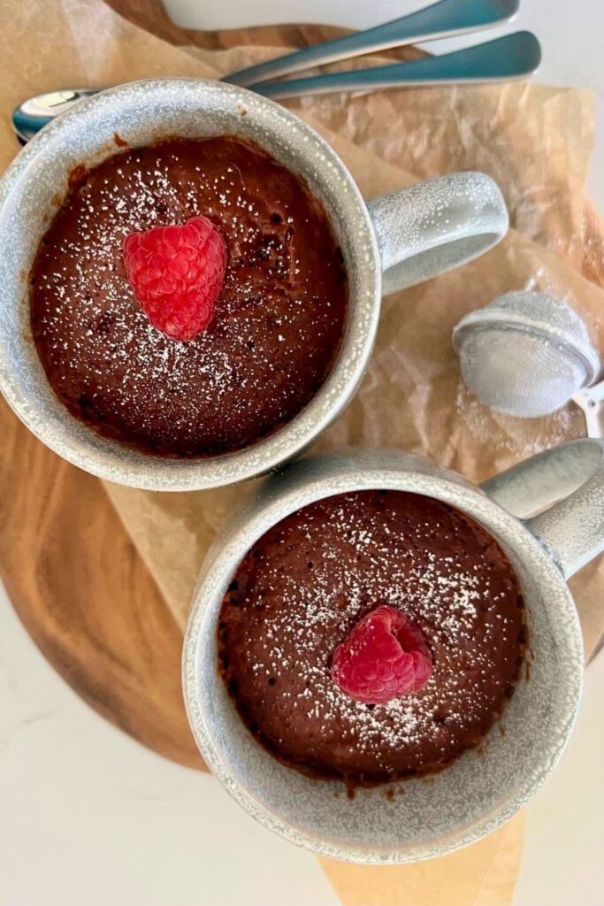 2 sourdough chocolate mug cakes that have been dusted with powdered sugar and topped with a fresh raspberry.