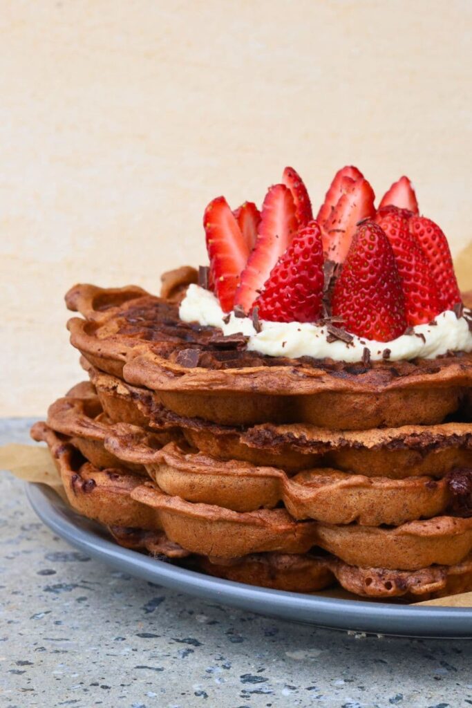 A stack of 4 sourdough chocolate waffles topped with whipped cream and fresh strawberries.