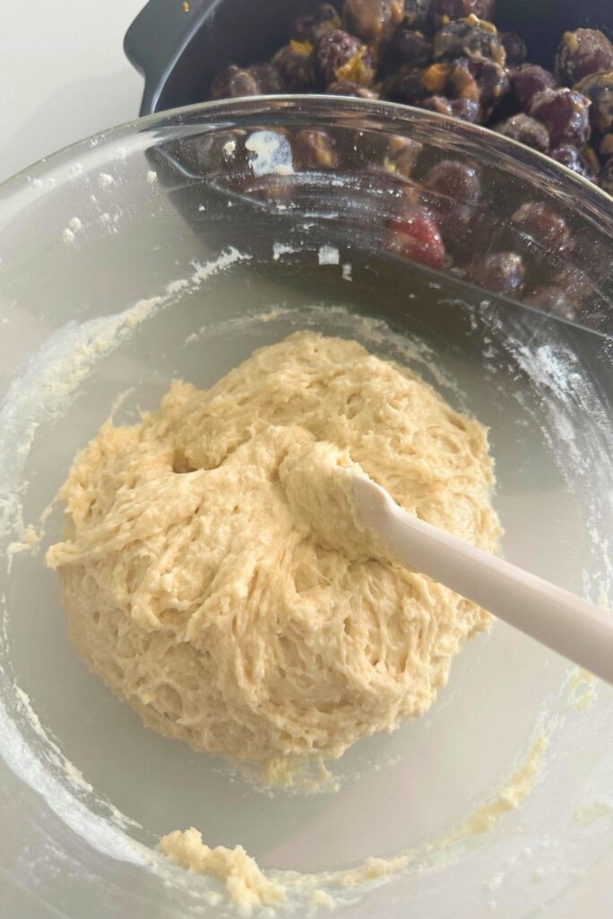 A glass bowl of sourdough cobbler batter ready to top a dish of cherries.