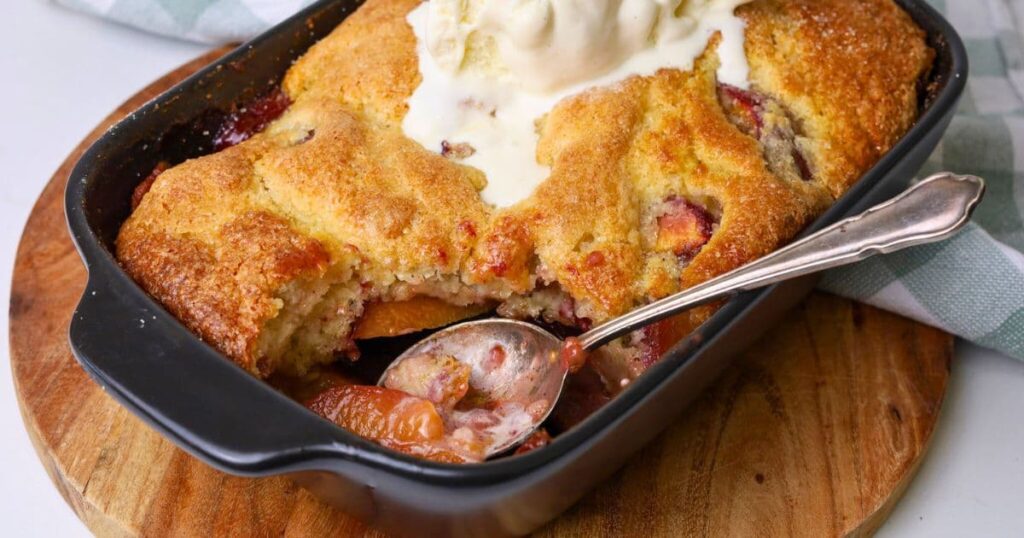 A horizontal image of a sourdough peach cobbler that has just been removed from the oven and topped with vanilla icecream.