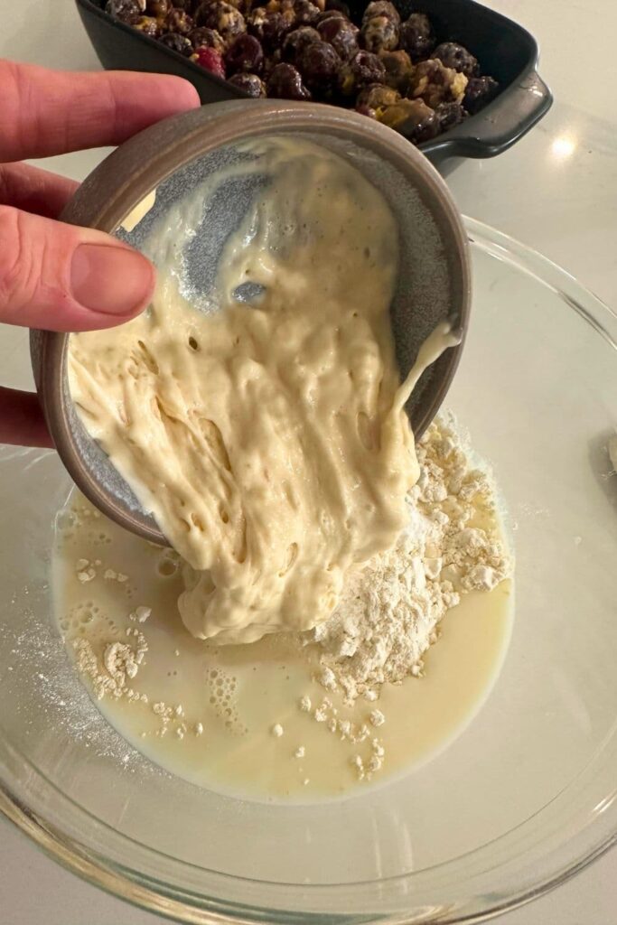 Pouring a bowl of sourdough starter into a bowl of other wet and dry ingredients.