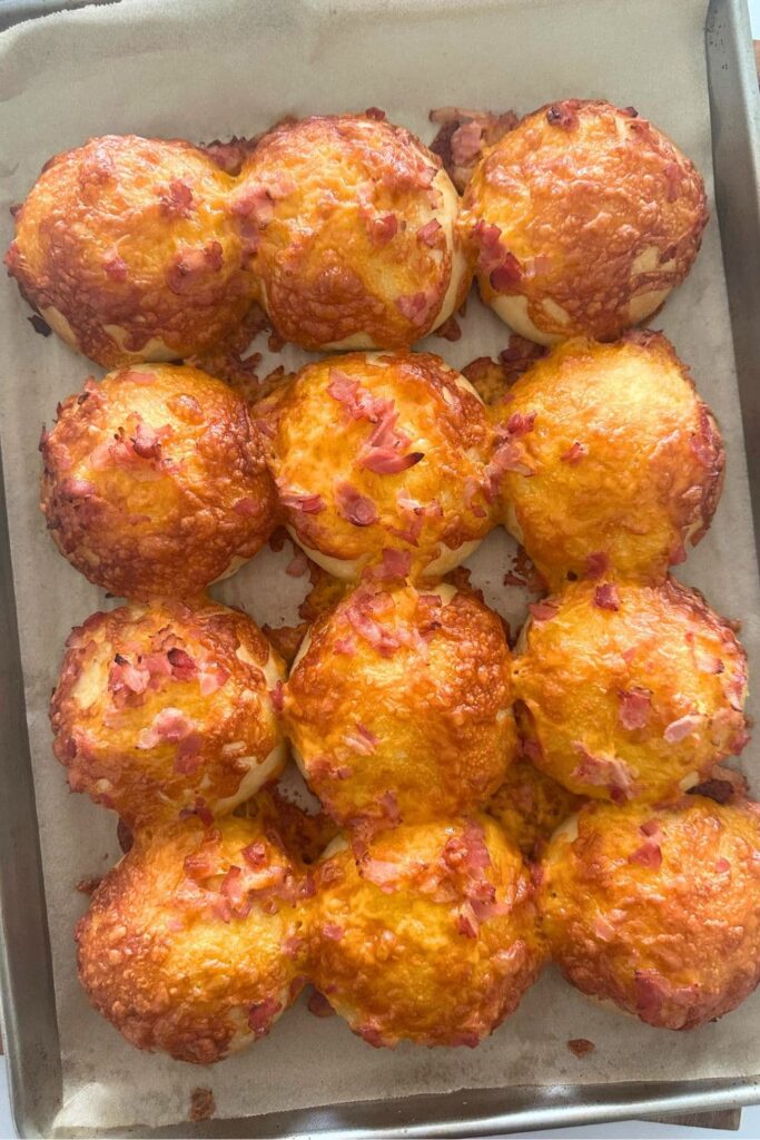 A tray of sourdough bacon and cheese buns that has just come out of the oven so the bacon is crispy and the cheese all melted and golden.