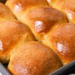 A baking tray filled with whole wheat sourdough dinner rolls that have been brushed with melted honey butter.