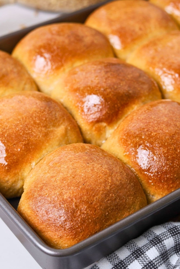 A baking tray filled with whole wheat sourdough dinner rolls that have been brushed with melted honey butter.