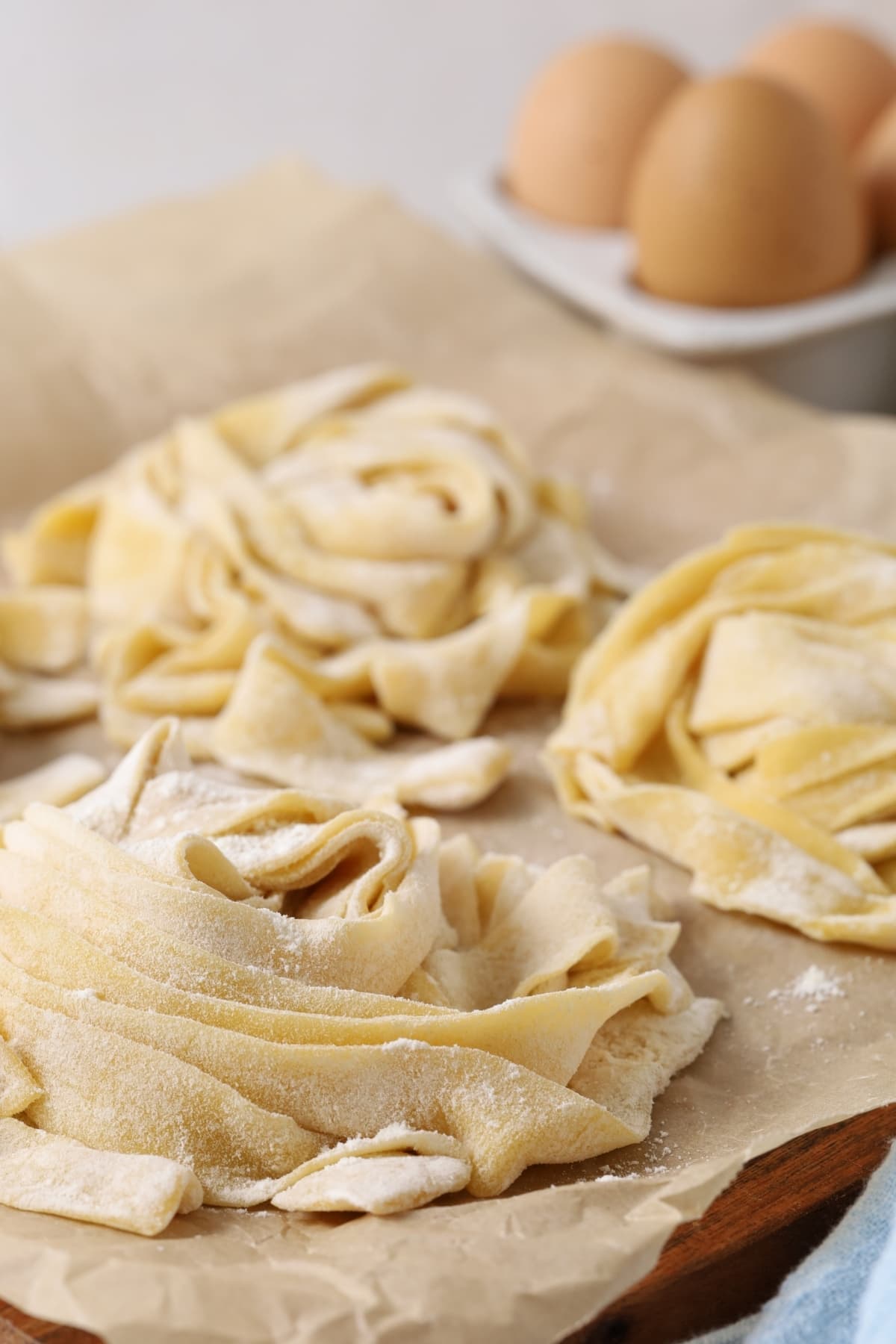 A close up image of nests of fresh pasta made using sourdough discard. There are 3 eggs in the background of the photo.