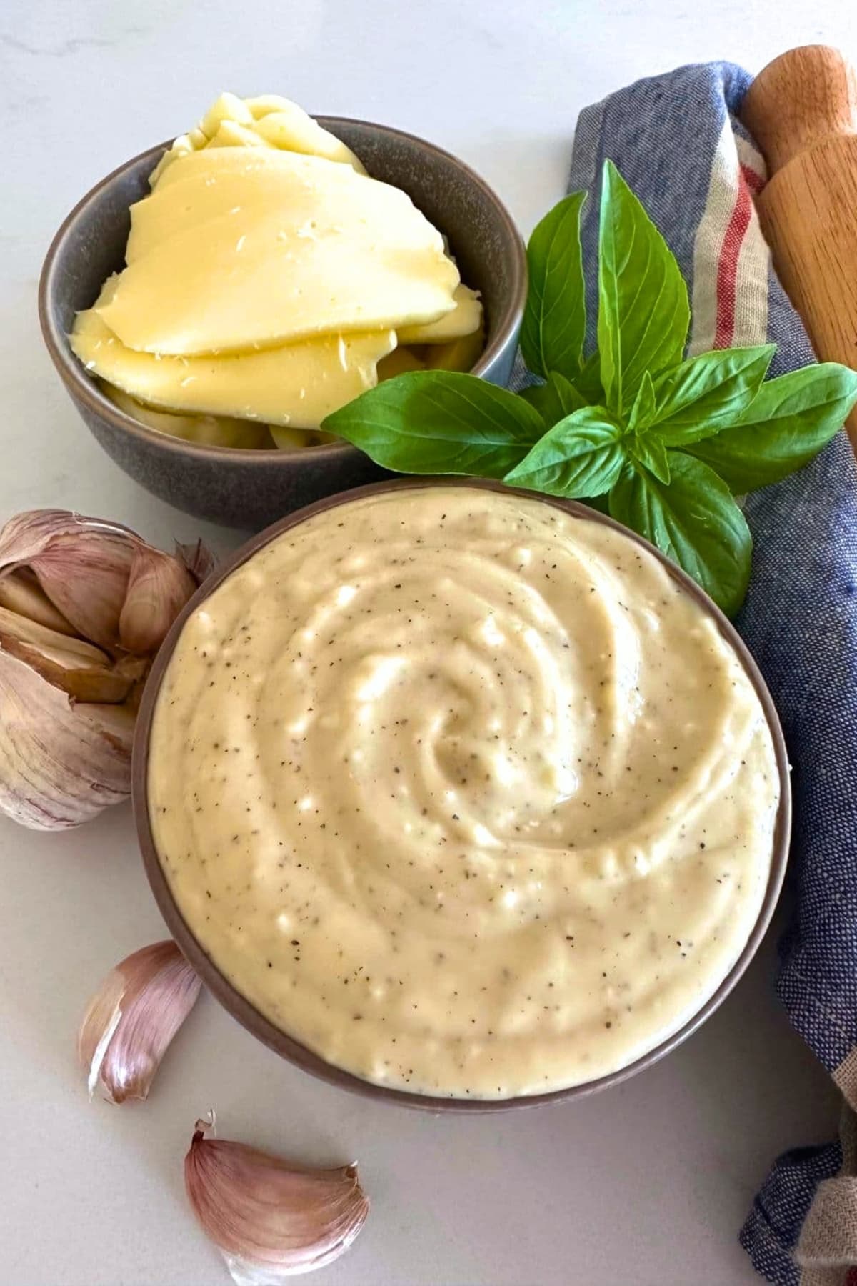 A bowl of white garlic pizza sauce adorned by fresh basil and mozzarella cheese.
