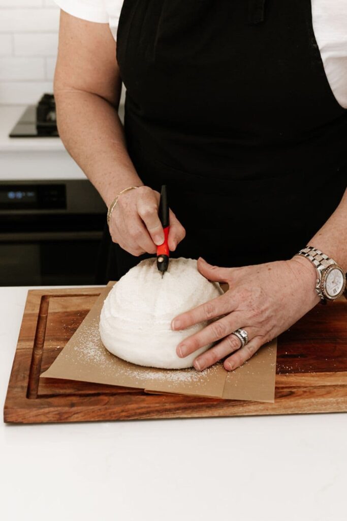 A loaf of sourdough bread being scored with a red handled lame.