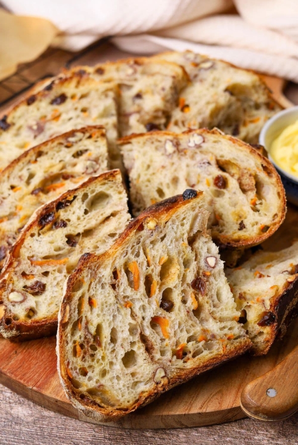 A sourdough carrot cake loaf that has been sliced up and displayed on a wooden board.