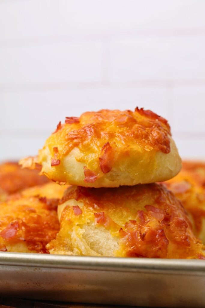 Two sourdough cheese and bacon rolls sitting on top of one another in a baking tray.