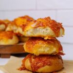 A stack of 3 sourdough bacon and cheese rolls showing the top roll with a bite taken out of it.