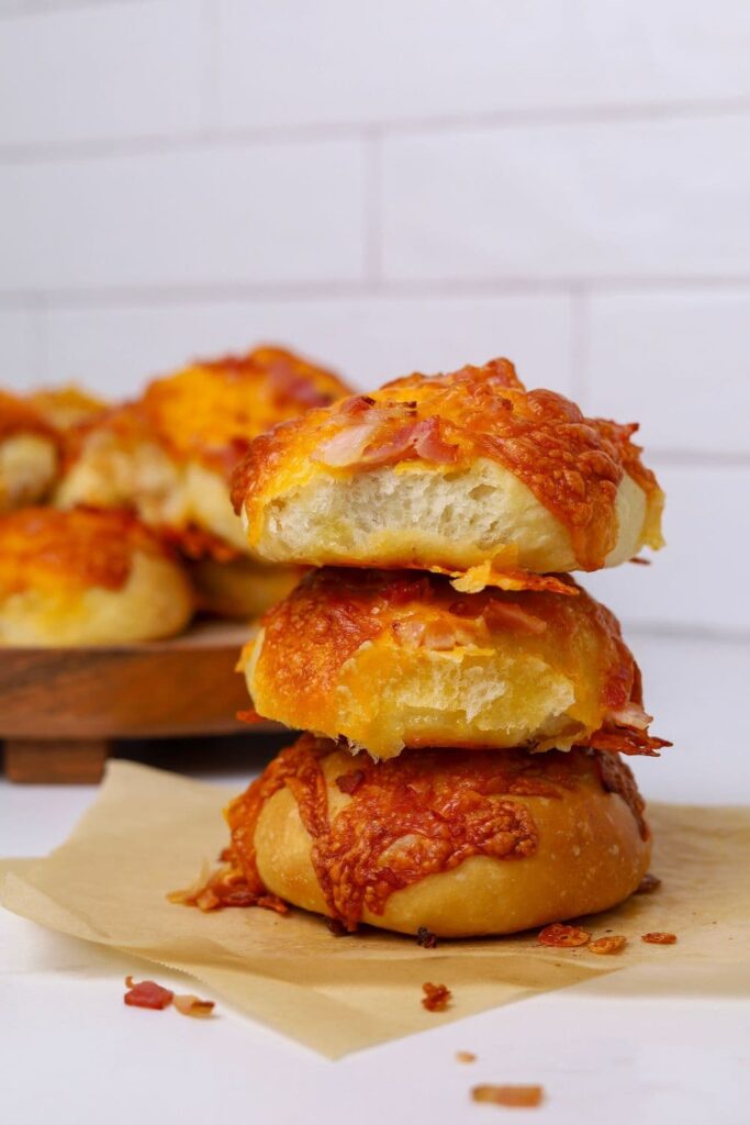 A stack of 3 sourdough bacon and cheese rolls showing the top roll with a bite taken out of it.