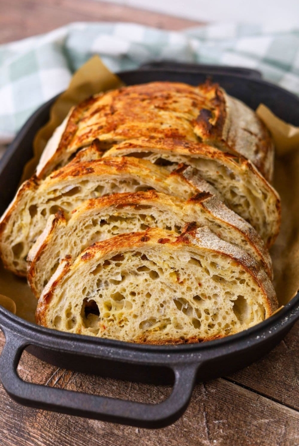 A loaf of sourdough with Italian herbs and cheese that has been sliced and laid out in a black cast iron bread pan.
