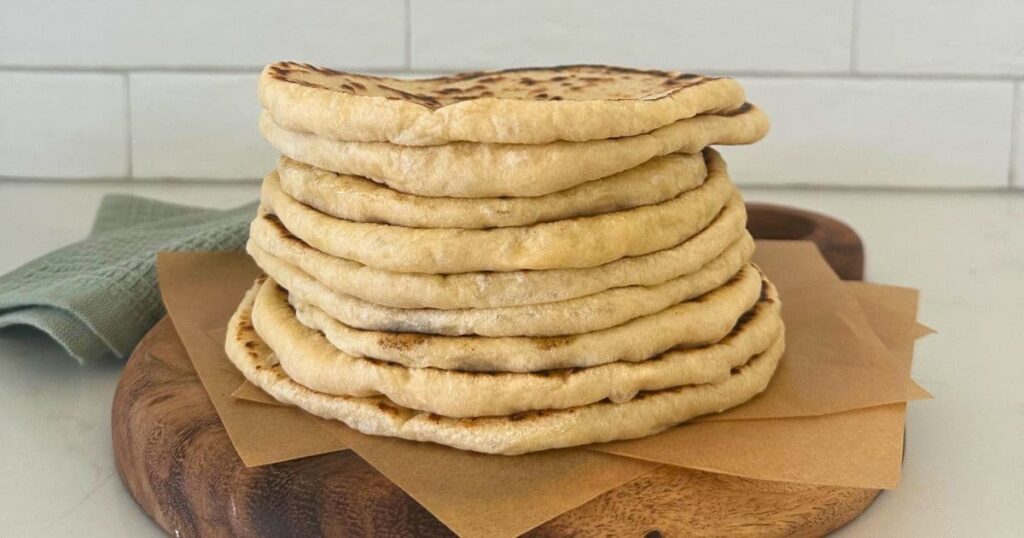 A stack of sourdough pita bread sitting on a wooden board.