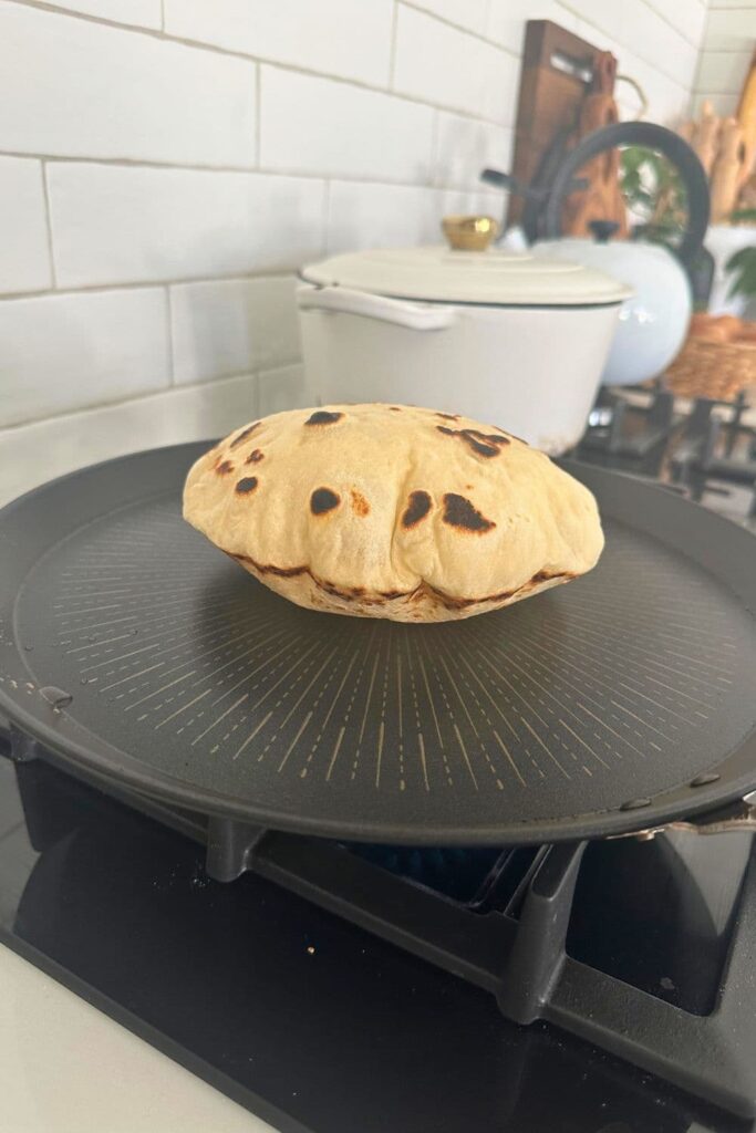 A sourdough pita bread puffing up on a hot skillet.