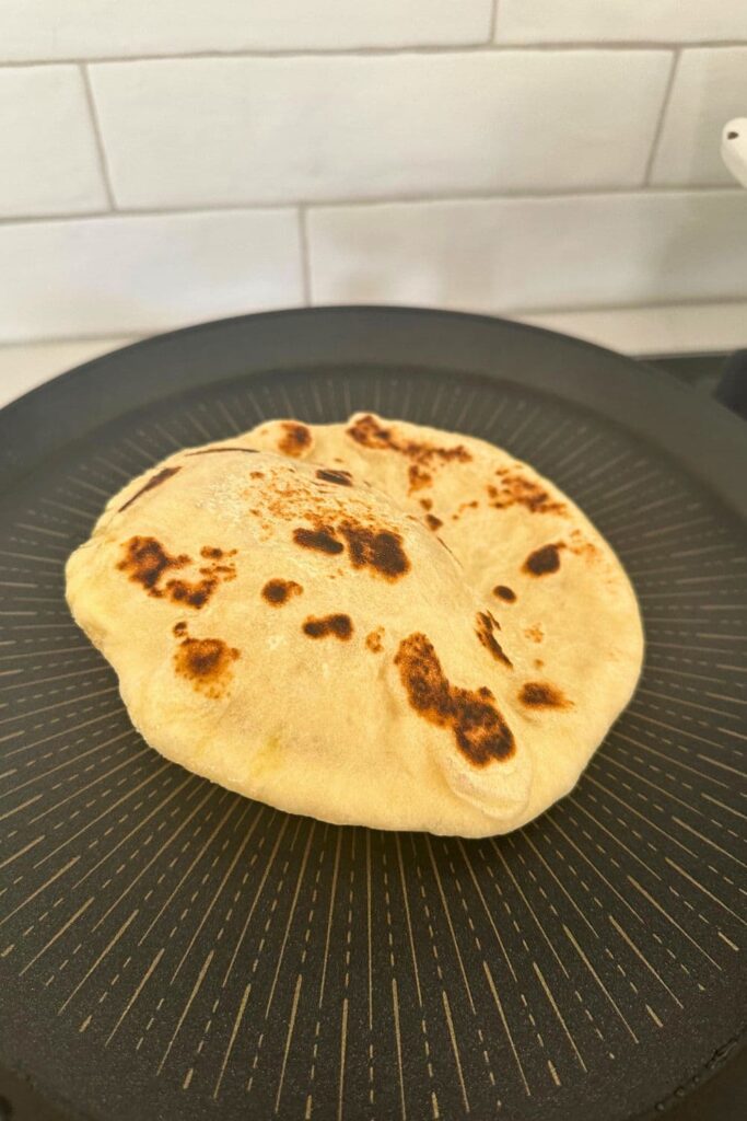 A sourdough pita bread being puffed up on a hot skillet.