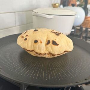 A sourdough pita bread being cooked on a non stick skillet that has puffed up.