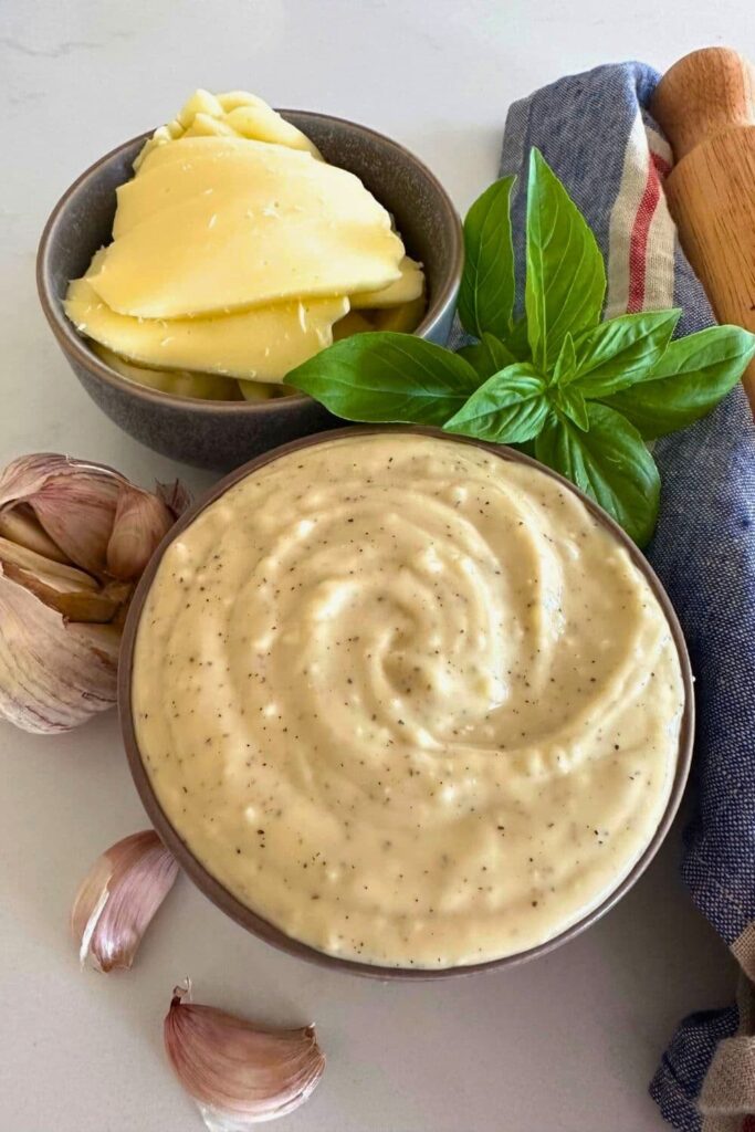 A bowl of white garlic pizza sauce adorned by fresh basil and mozzarella cheese.