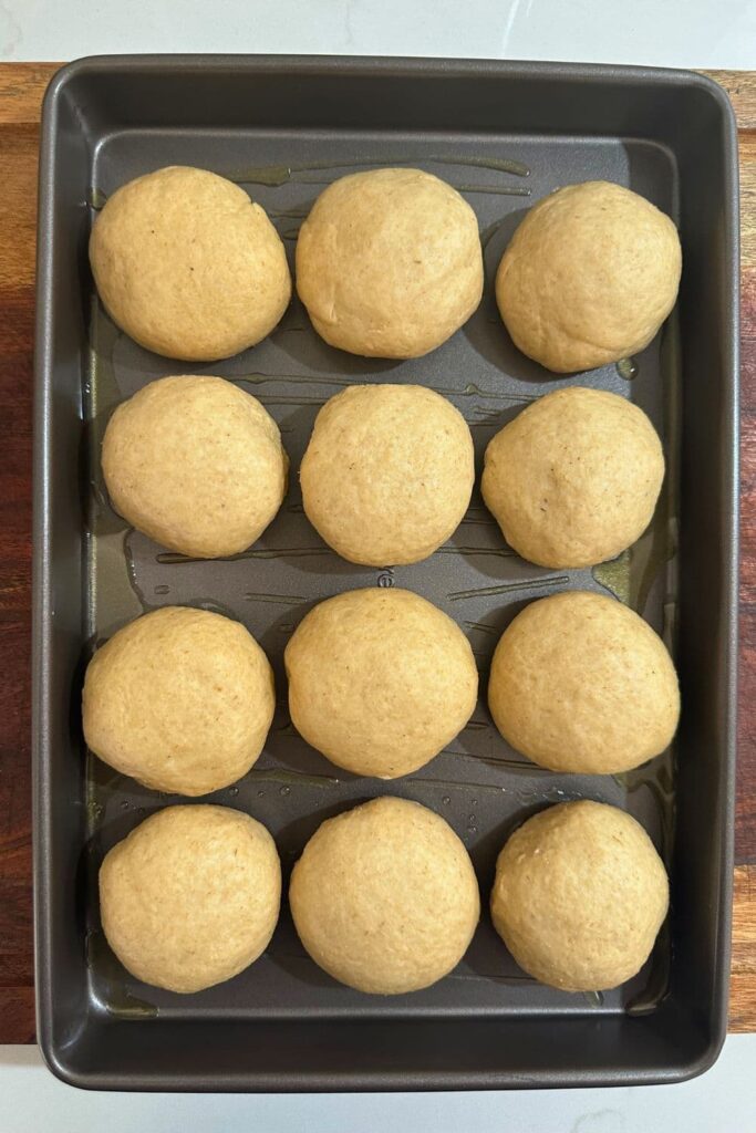 A rectangle metal baking pan containing 12 whole wheat sourdough dinner rolls.