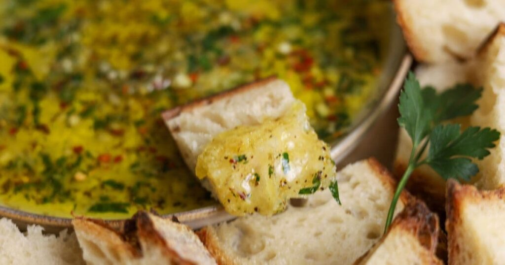 Close up photo of a piece of sourdough bread dipped in a plate of bread dipping oil.