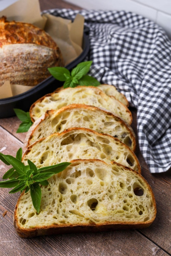 4 slices of sourdough mozzarella pesto bread laid out on a wooden table. You can see the rest of the loaf sitting in the background of the photo. The loaf is garnished with fresh basil leaves.