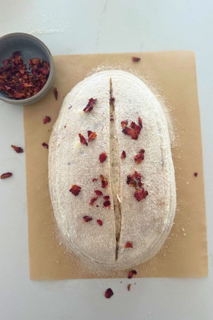 An unbaked loaf of sourdough that has been scored and sprinkled with dried rose petals.