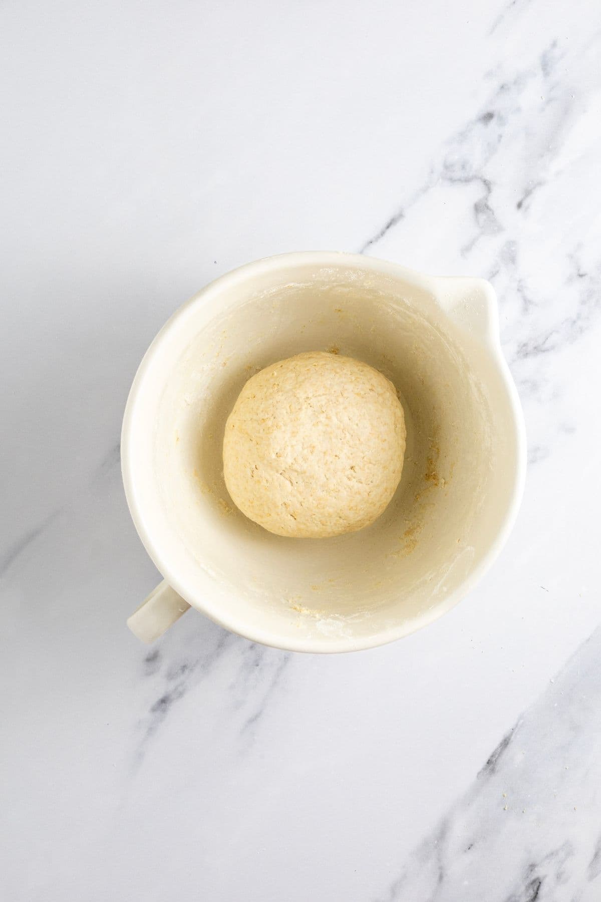 A medium sized cream batter jug filled with a ball of smooth dough for making whole wheat sourdough crackers.