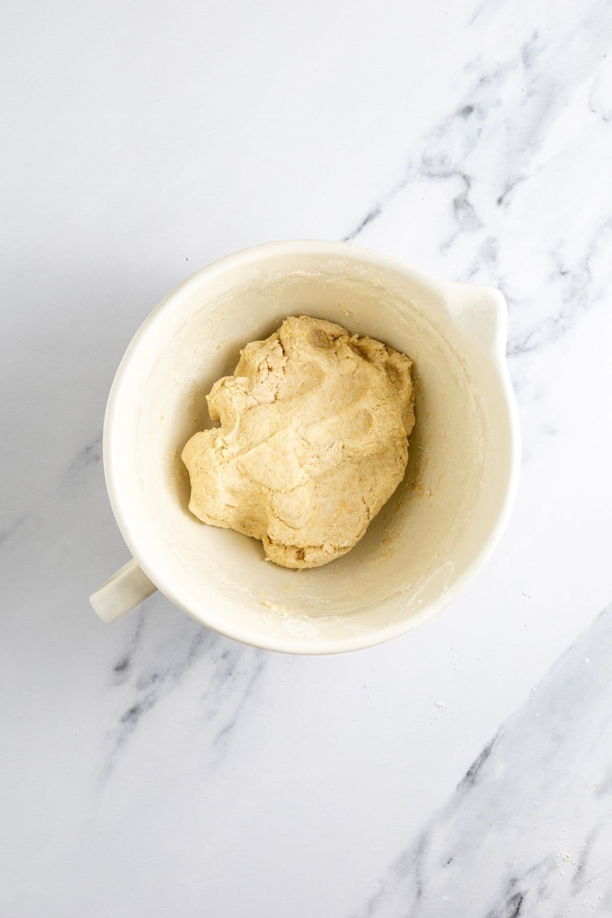 A medium sized cream batter jug filled with a rough dough for making whole wheat sourdough crackers.