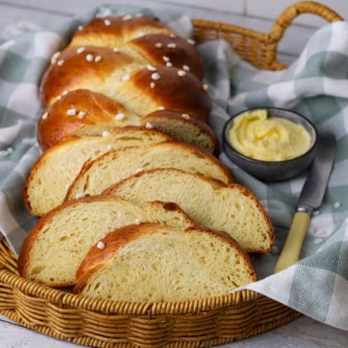 A loaf of sweet braided sourdough bread that has been sliced up and displayed in a basket next to a small dish of butter.
