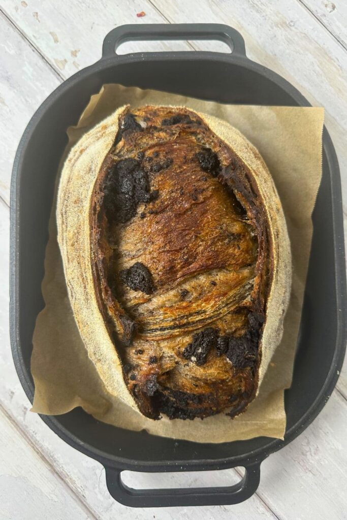 A loaf of cookies and cream sourdough bread that has been baked and taken out of the oven. It's sitting in a cast iron bread pan.