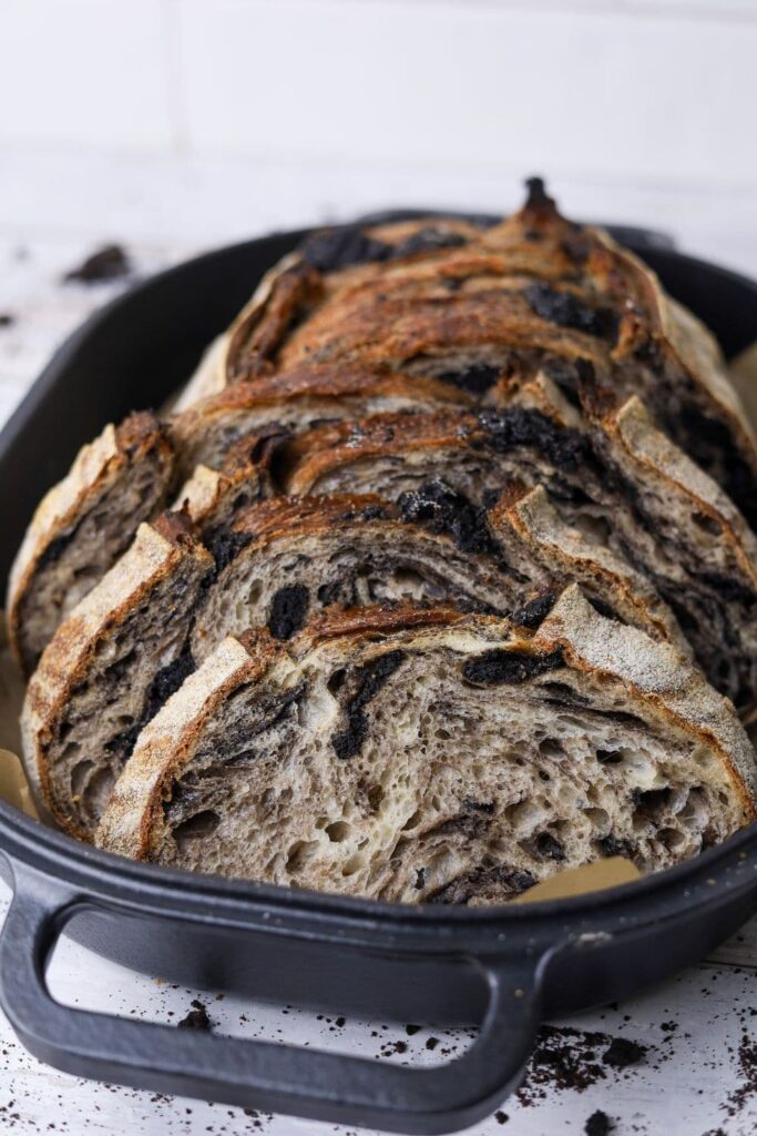 A loaf of cookies and cream sourdough bread that has been sliced and displayed inside a cast iron bread pan.