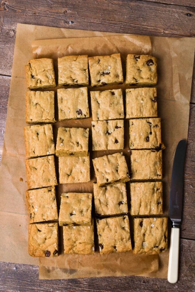 A whole batch of sourdough chocolate chip cookie bars cut into squares. The photo is taken from above so you can see all 24 bars. There is a white handled knife sitting next to the bars.