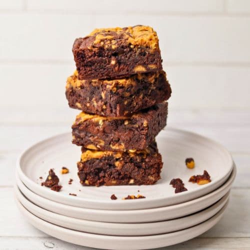 A stack of sourdough peanut butter brownies sitting on 4 white plates. The brownies are stacked haphazardly so you can see all the angles.