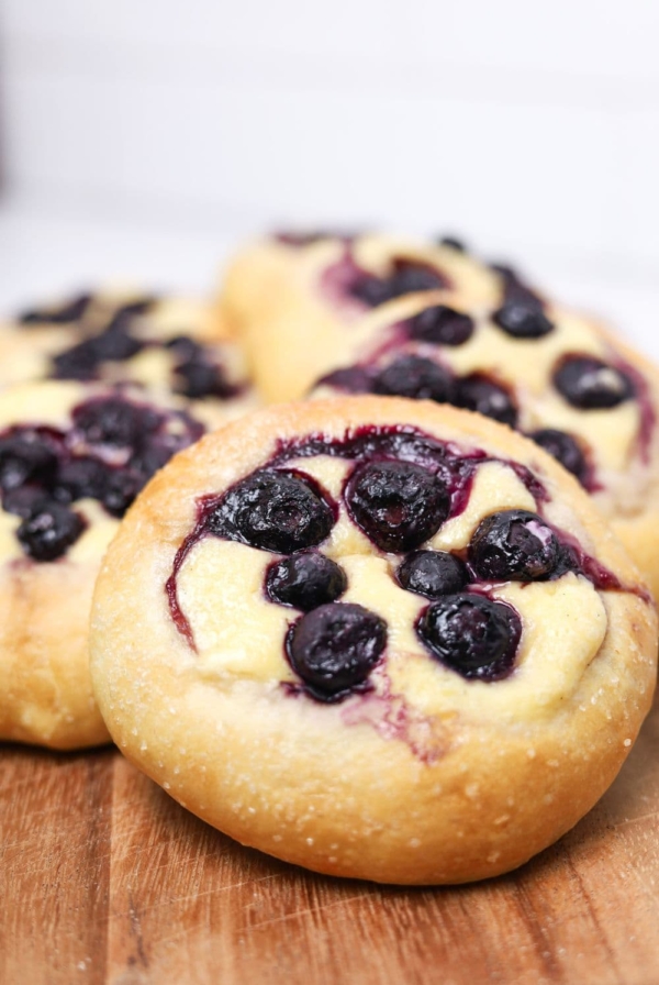 A close up photo of a sourdough blueberry brioche roll filled with vanilla cheesecake filling and topped with juicy blueberries.