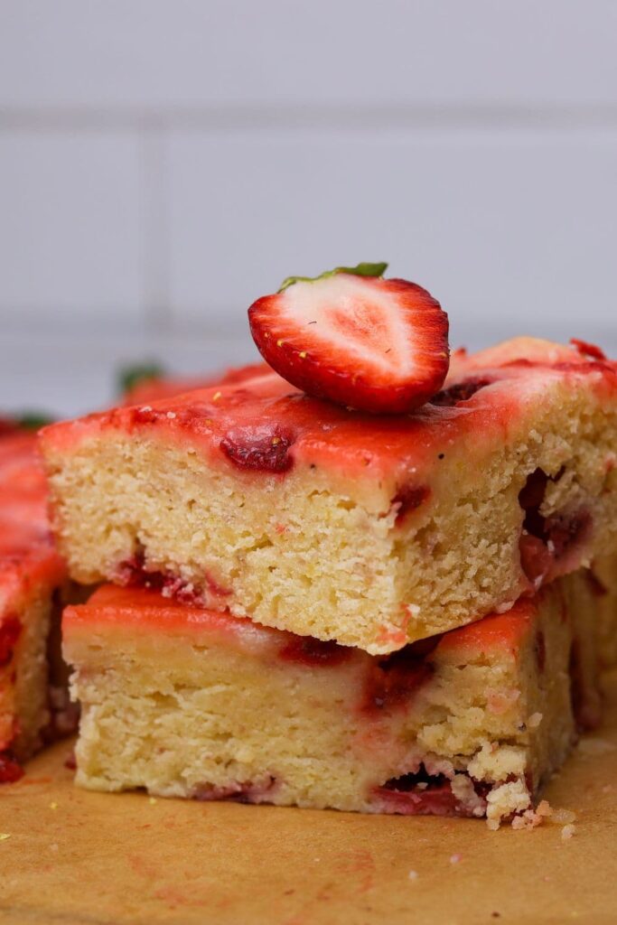 A close up photo of sourdough strawberry bars showing 2 stacked on top of each other. You can see the bright red strawberries and yellow lemon zest peaking through the golden crumb.