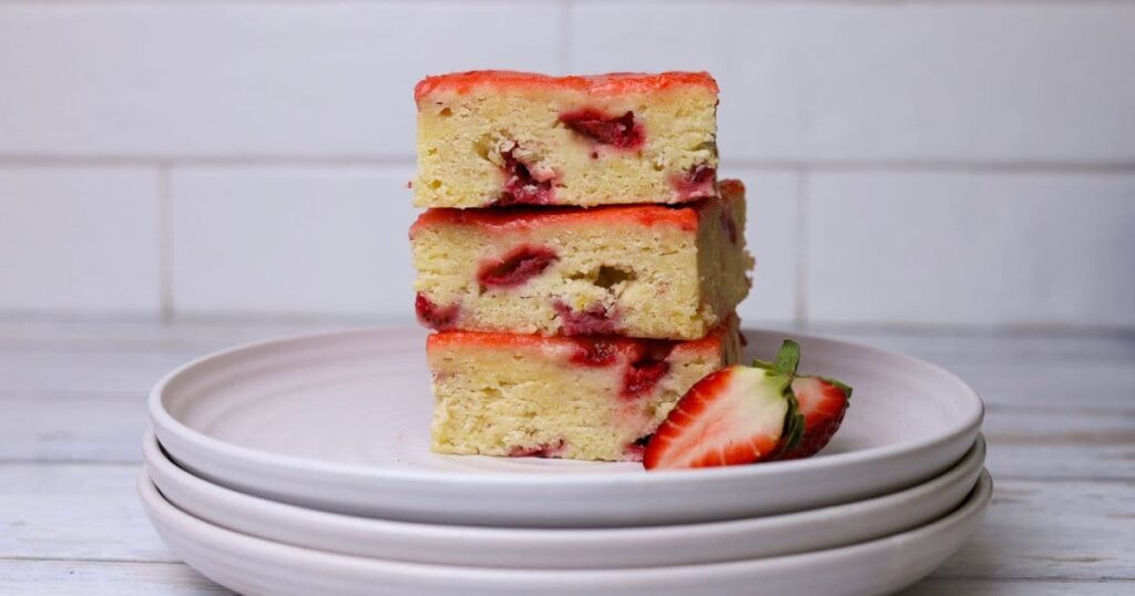 3 sourdough strawberry bars stacked on top of each other on a stack of white plates.