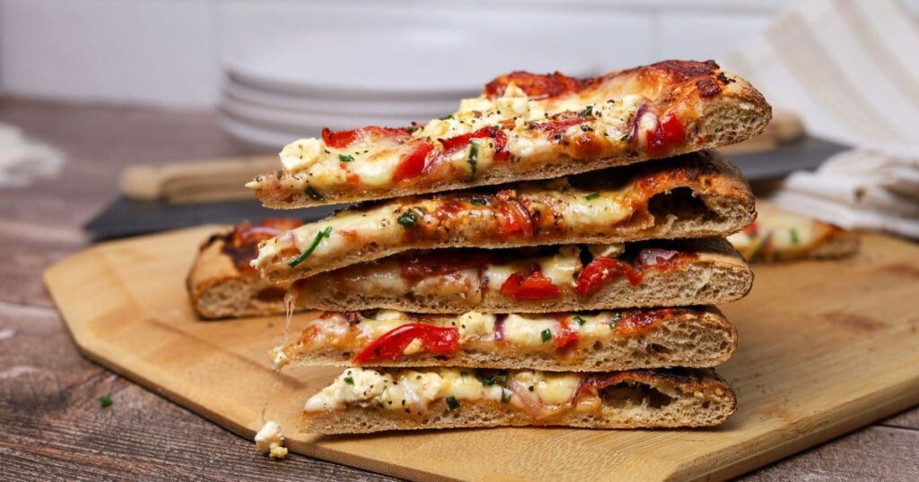 A stack of whole wheat sourdough pizza slices topped with mozzarella and vegetables.