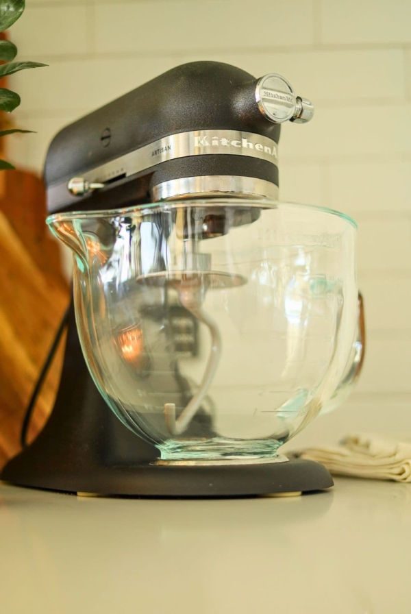 A matte black KitchenAid Artisan Stand mixer with a glass bowl and dough hook attached.