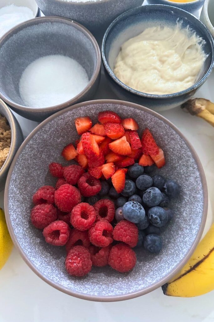3 bowls, one containing white sugar, one sourdough starter and the larger bowl contains fresh raspberries, blueberries and diced strawberries. You can also see a banana in the photo too.