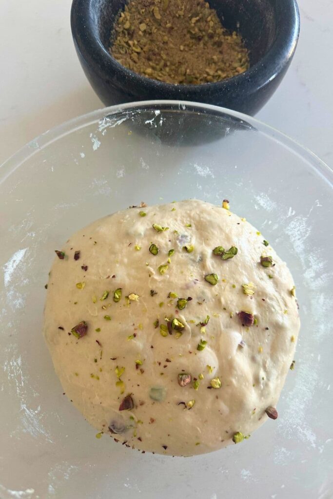 A glass bowl of sourdough pistachio dough that has finished bulk fermentation and is bubbly and domed on the top.
