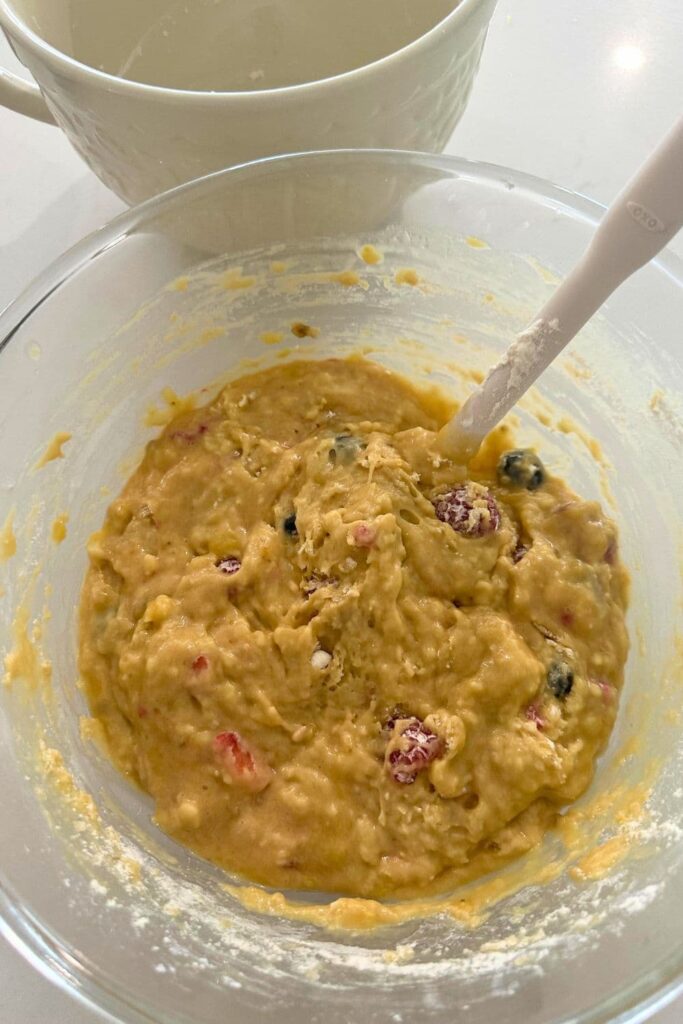 A glass bowl filled with sourdough berry banana bread batter. There is a white spatula in the bowl that has been used to mix the batter.