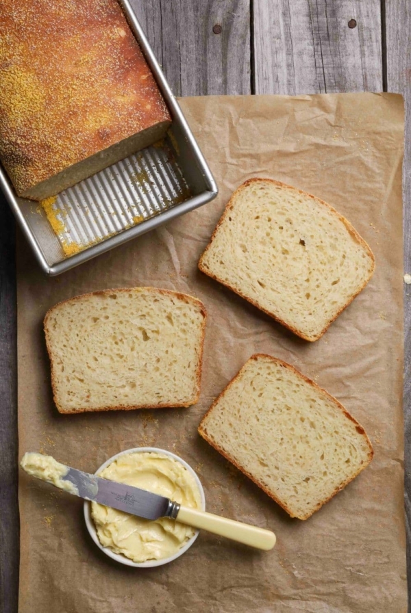 Sourdough English muffin loaf on parchment paper with three slices of bread ready to be buttered.