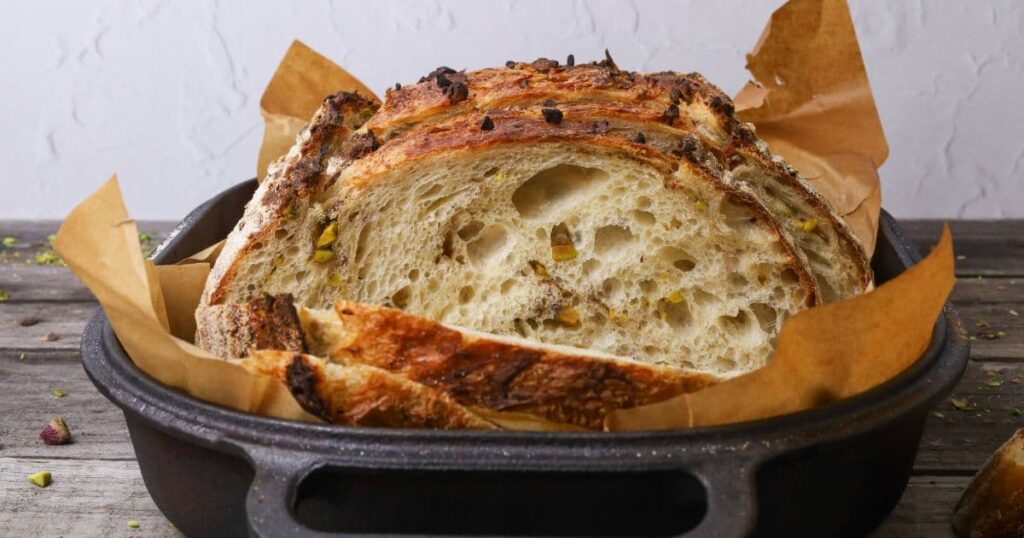 A loaf of pistachio sourdough bread that has been sliced. The photo is taken front on to show the open crumb and pistachio nuts laced through the sliced sourdough bread.