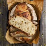 A loaf of sourdough pistachio bread photographed from the top down showing a slice laid open so you can see the crumb inside.