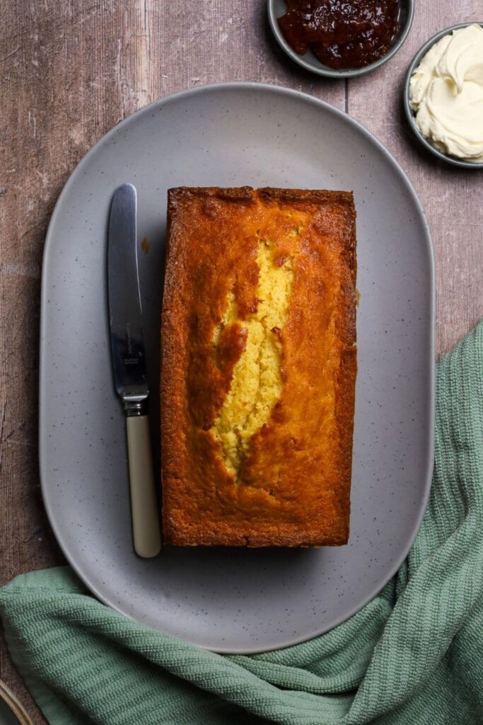 Whole sourdough pound cake sitting vertically on a plate. The photo is taken from above so you can see the golden brown top of the cake as well as the split on the top where the yellow cake is peaking through.