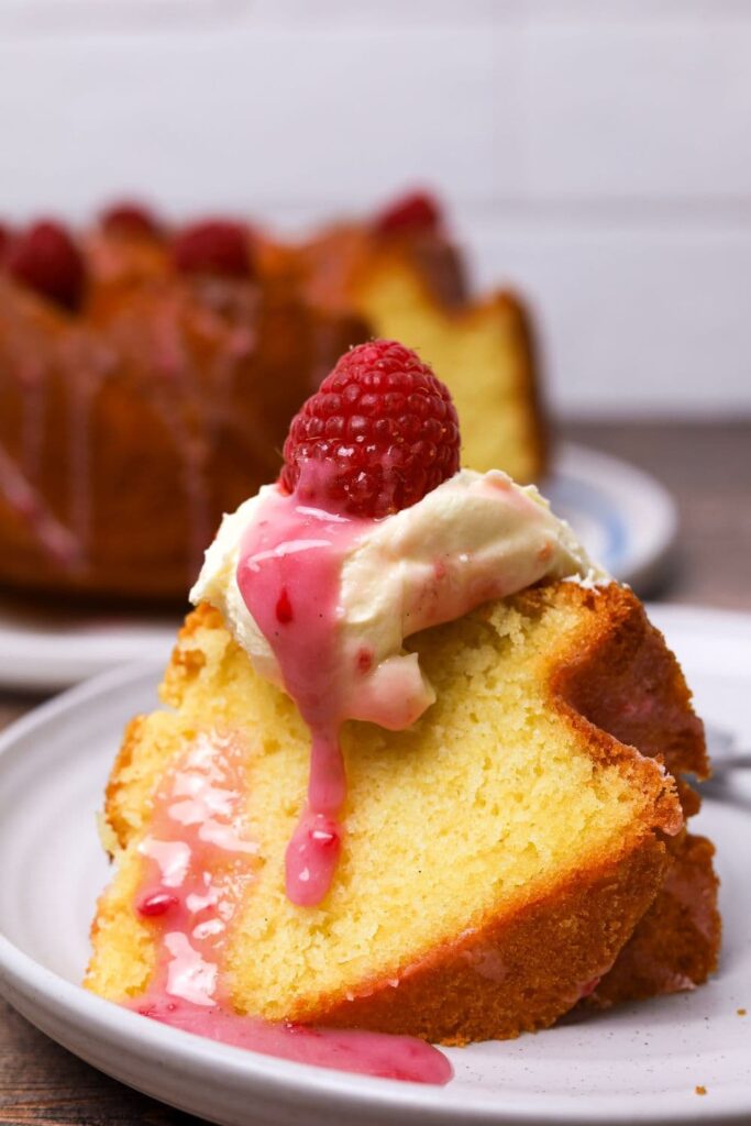 sourdough pound cake slice with butter, glaze and a raspberry on a plate.